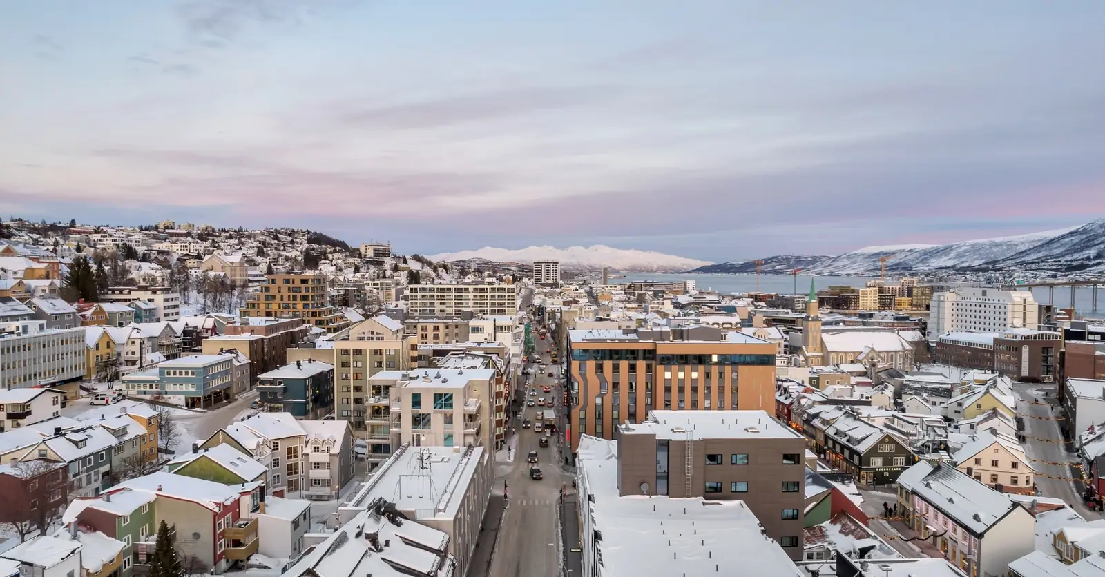 Tromsø sentrum i rosa vinterskumring, med snødekte fjell bak